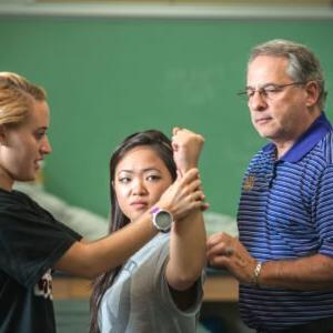 A student performs a physical therapy check while a professor observes.
